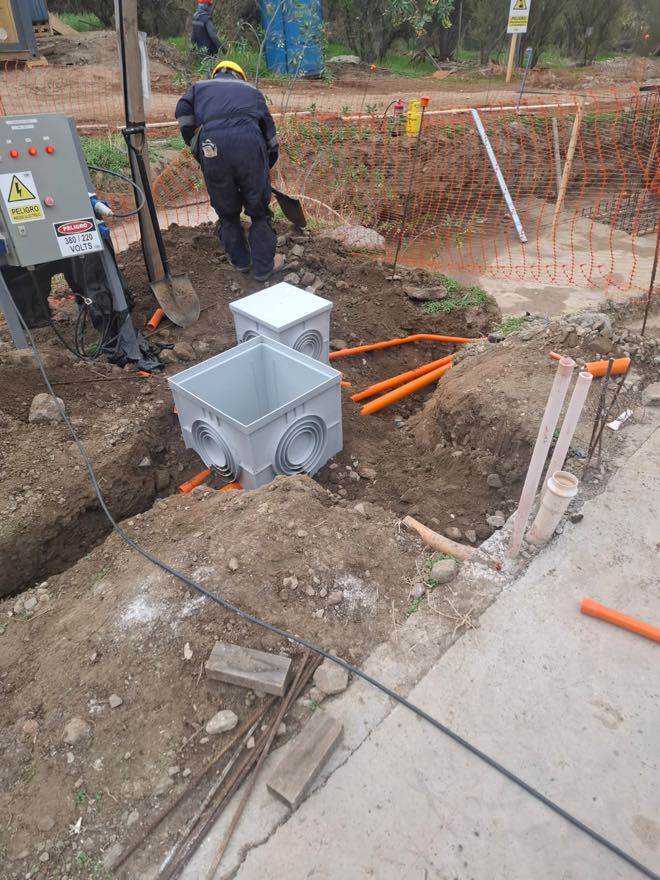 Dos cámaras de registro eléctricas instaladas en zanja con los ductos llegando a sus entradas, junto al tablero provisorio de faena